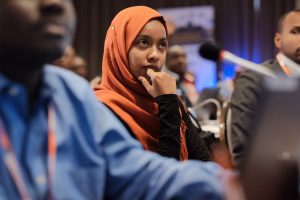 une femme portant un foulard assise lors d'un événement écoutant