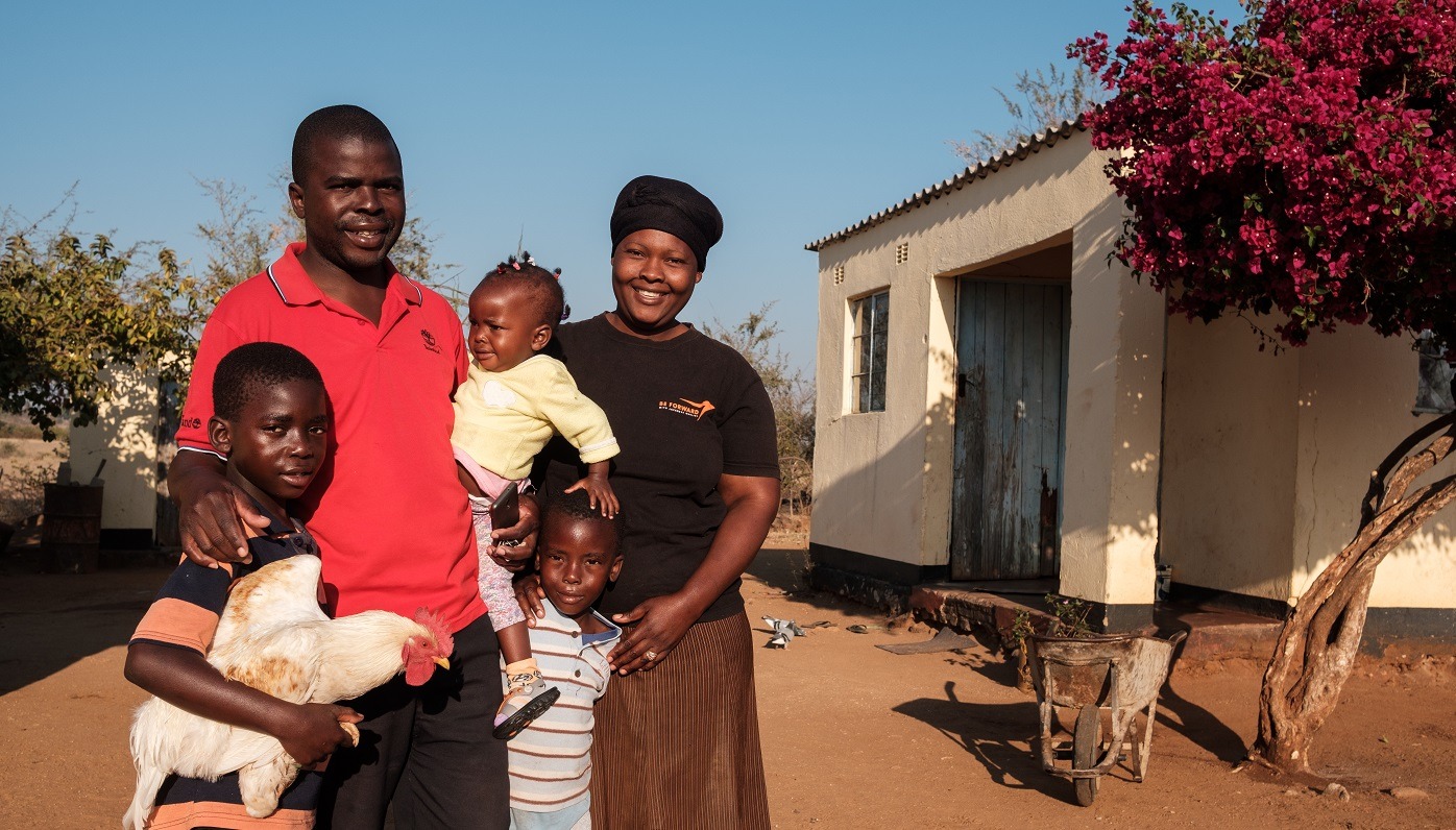 A man and a woman with three kids, one of which is holding a rooster, posing for a photo