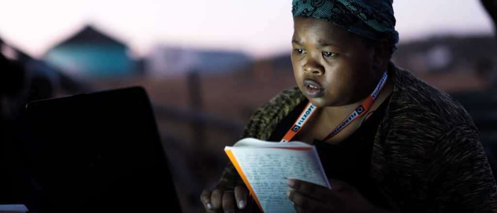 A woman holding a notebook and looking at the laptop