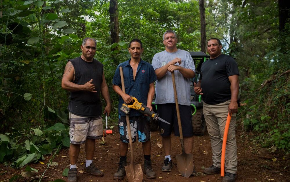 Cuatro hombres parados en el bosque con palas y una sierra.