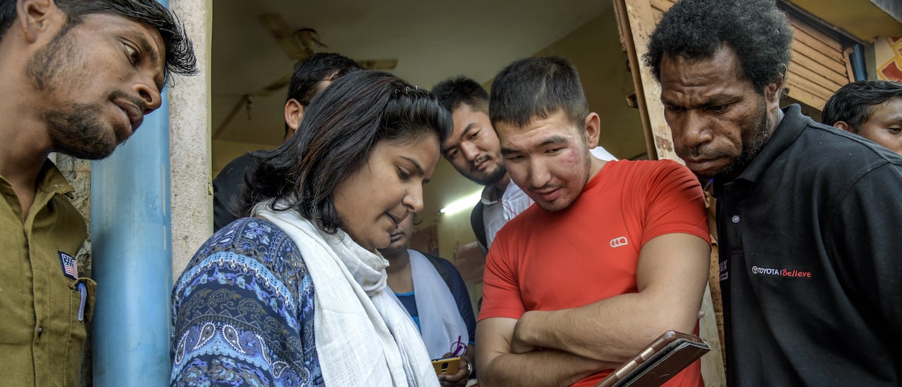 A woman holds a tablet while a group of people look at it together in India