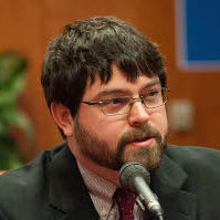 A headshot of a man speaking with the microphone