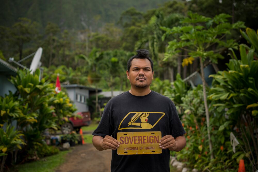 a man holding 'Sovereign Kingdom of Hawaii' yellow sign