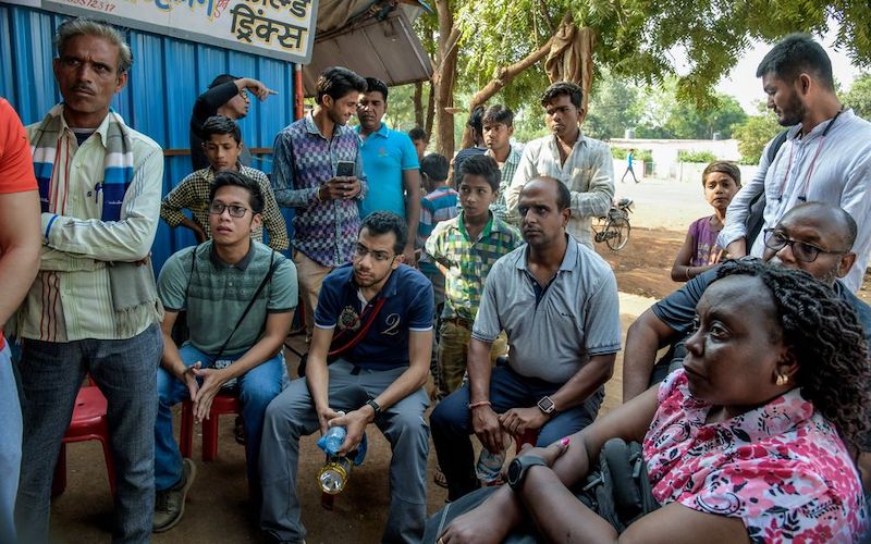 un grupo de hombres y una mujer de la India sentados o de pie mientras escuchan a alguien