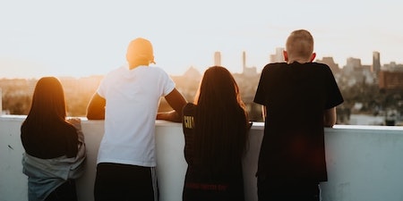 Two girls and two boys standing on the roof and looking at a city in the distance