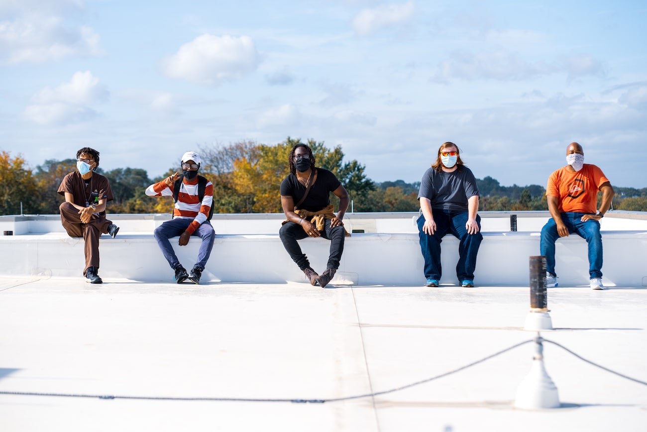 Five men sitting on the small wall wearing face masks