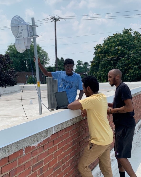 Three men on the roof with laptop and antenna 