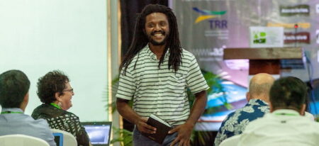 Man with long hair smiling while walking between people sitting at an event