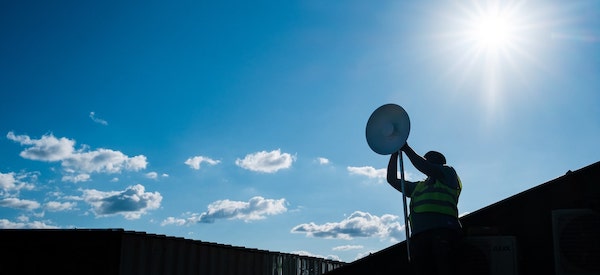 un hombre con las manos en alto mientras instala una antena bajo el sol
