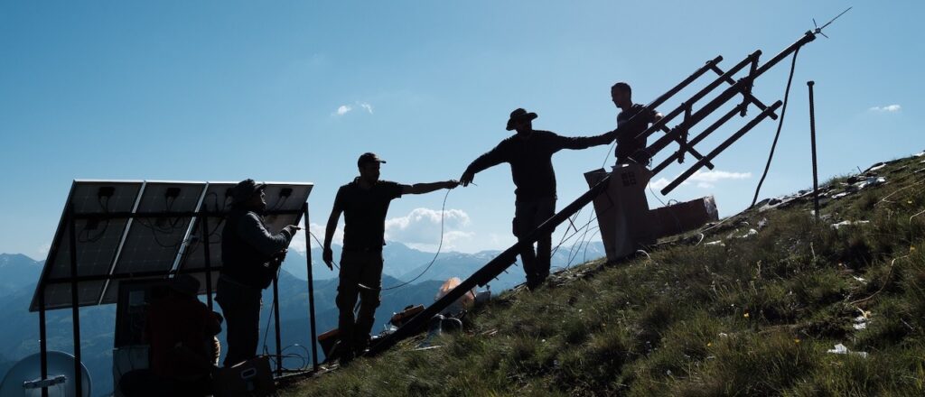 a group of people installing antenna and solar panel on top of a hill