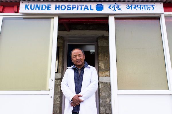 a man wearing black doctor coat standing at the entrance of a Kunde hospital