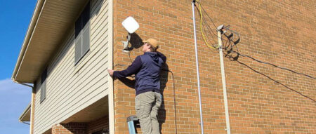 a man standing on a ladder installing Internet hardware