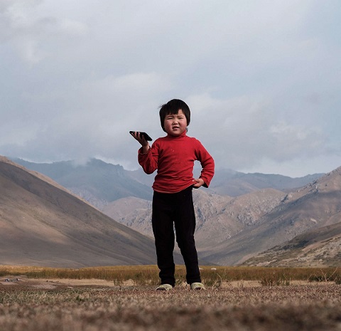 A child holding a phone and standing in the valley