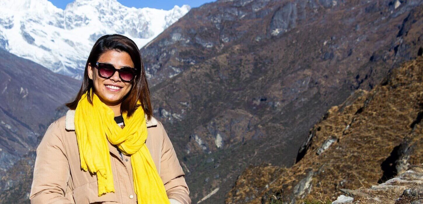 a woman smiling at camera in front of mountain peak