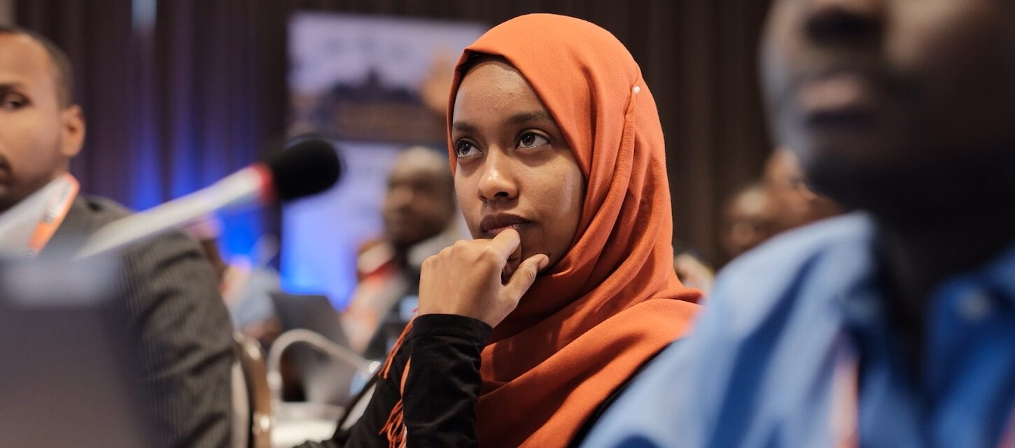 a woman in a headscarf sitting at an event listening