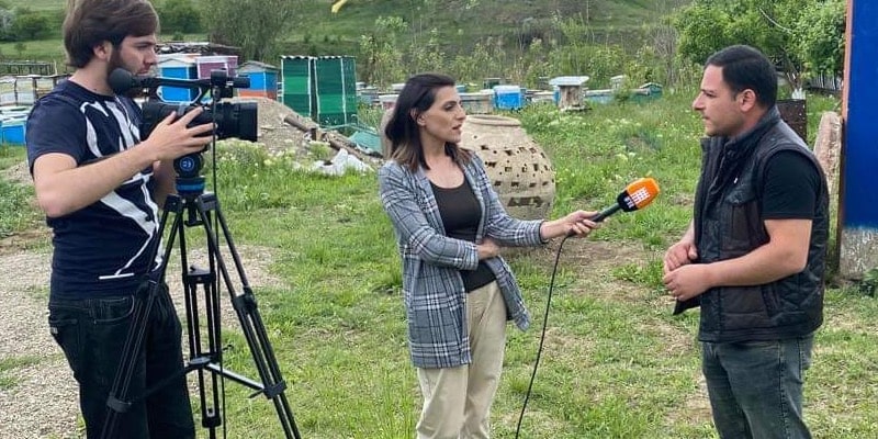 Cameraman on left filming female reporter (middle) and male interview subject on the right.