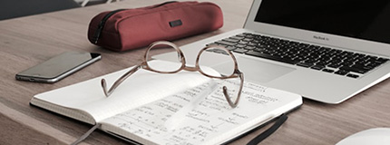 Laptop on the table together with notebook, glasses, mobile phone and a pencil case