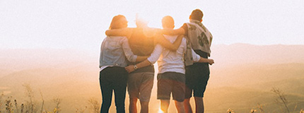 A picture of four people from the back who are hugging and looking at the sunset