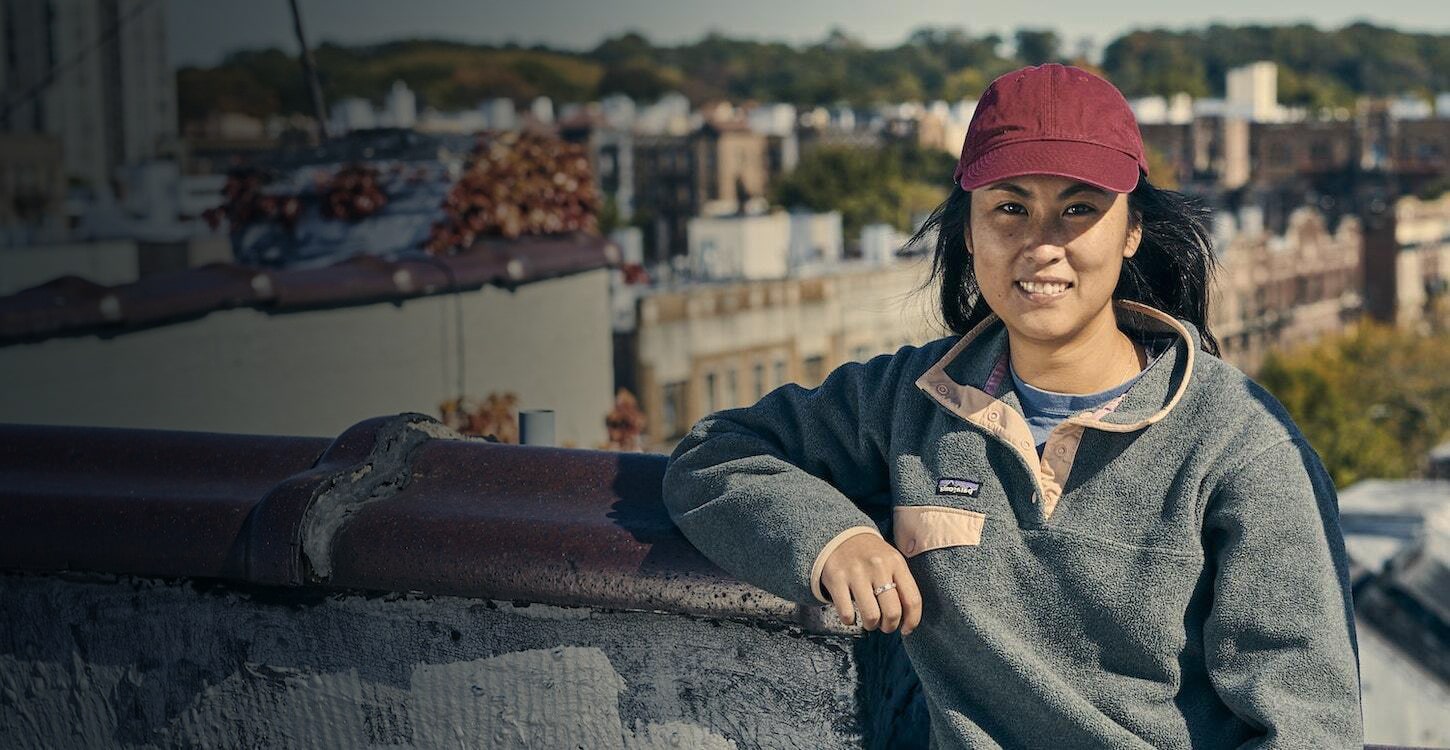 a woman with a red cap leaned on a wall at the top of a building smiling