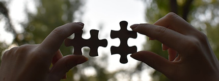 Female hands holding 2 pieces of the puzzle in the background of trees
