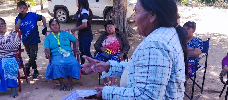 una mujer sosteniendo papeles explicando a otras mujeres que están sentadas escuchando