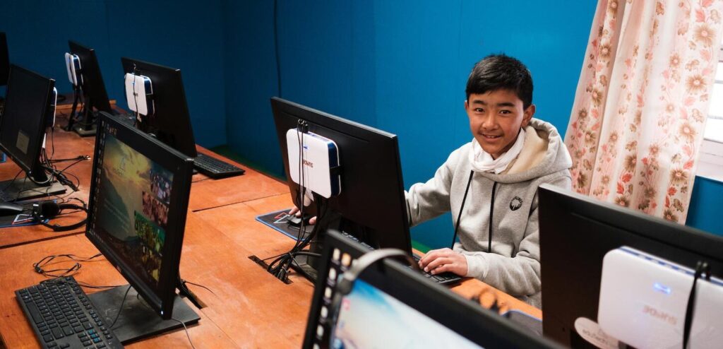 a boy sitting in front of the computer in a classroom smiling