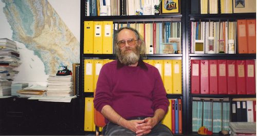 a man with a grey beard and glasses sitting in the office 