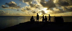 Silhouettes of people standing in front of the Ocean in Tuvalu at sunset.