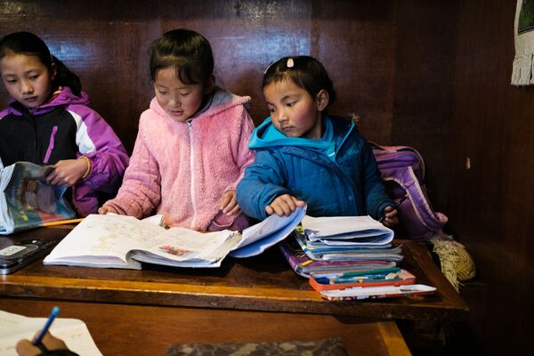 Three little girls studying from a school textbook in Nepal