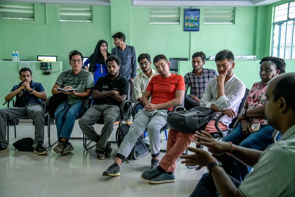 People sit around a semicircle attentively listening to a man talk