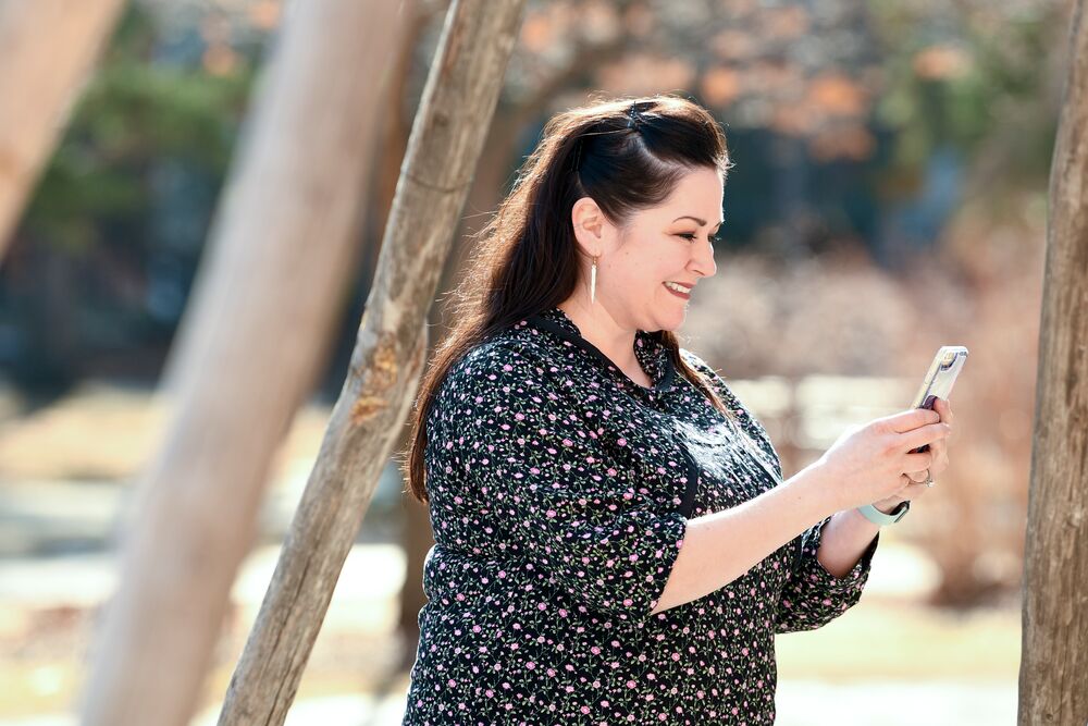 Une femme tenant un téléphone portable, envoyant des messages et souriant.