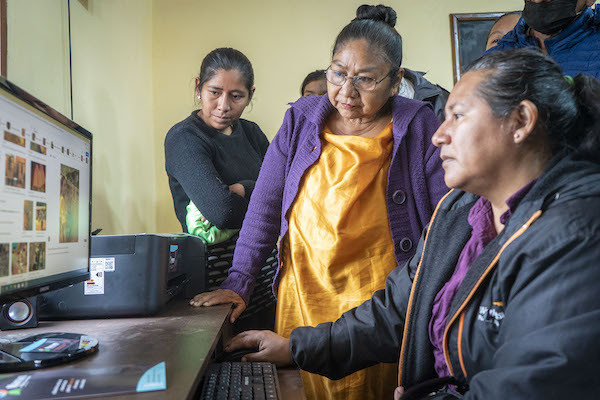 Several women stare at a computer screen in Bolivia