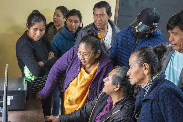 A group of women and men gather around a computer in Bolivia