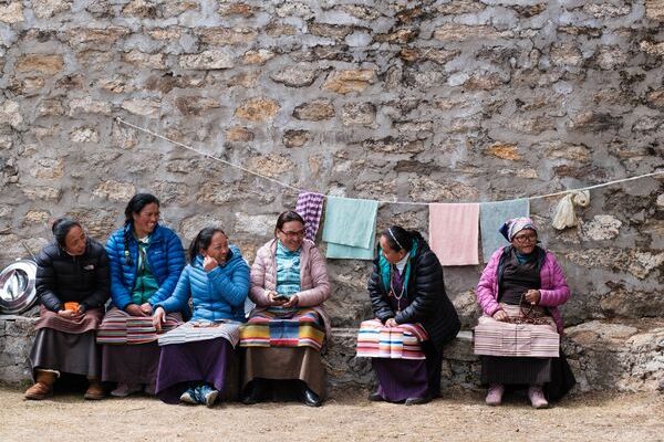 A group of women sitting side by side in front of a stone wall in Nepal