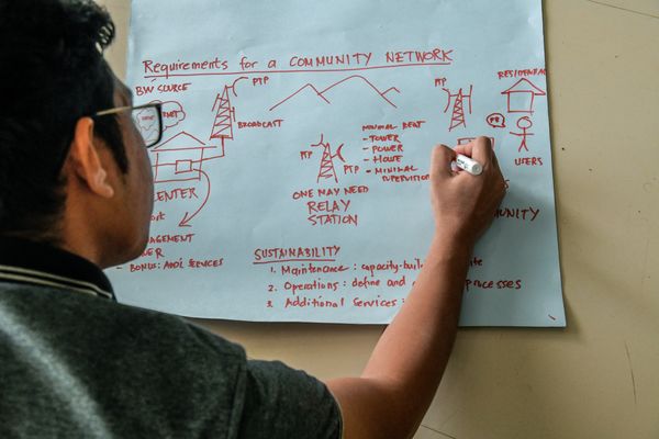 A man writes on a large paper on the wall where it’s possible to see drawings of a network structure