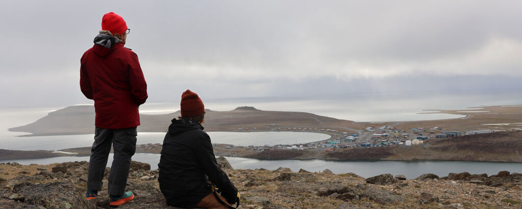 Dos personas en lo alto de una colina mirando hacia el horizonte con una ciudad y el océano a lo lejos.