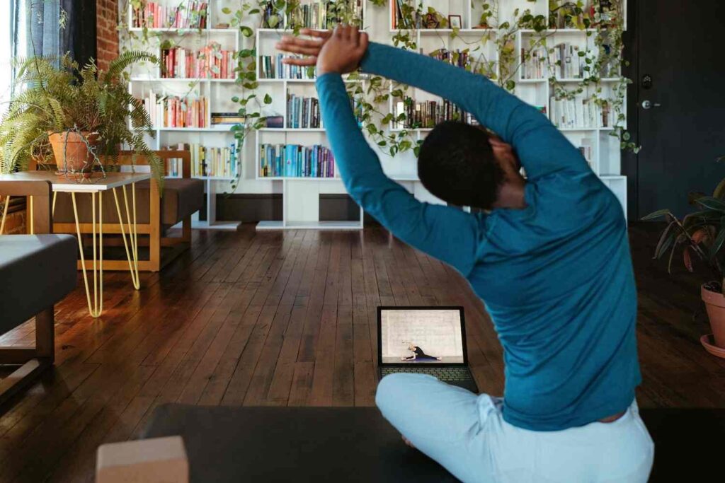 A man exercising yoga in front of a laptop