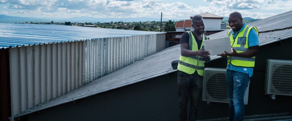 two men holding a laptop looking at the screen on a house roof