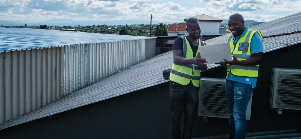 two men holding a laptop looking at the screen on a house roof