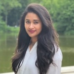 A woman in a white shirt standing in front of a serene lake.