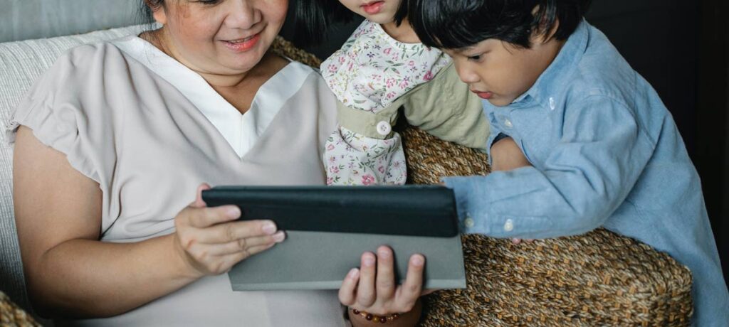 Woman sits with two children looking at a tablet.