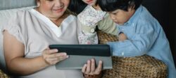 Woman sits with two children looking at a tablet.