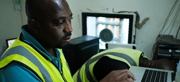 A man in a safety vest is focused on his laptop