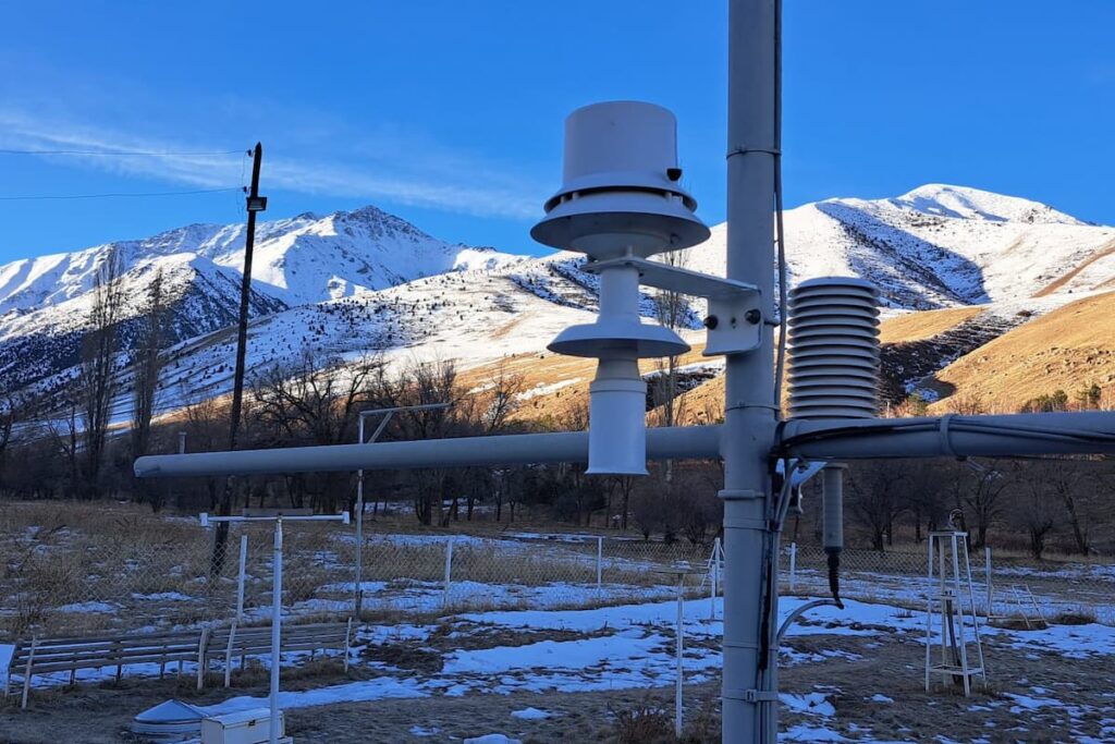 Weather monitoring infrastructure in Kyrgyzstan with snow-covered mountains in background.