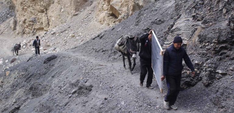 A few people and a donkey carry equipment up a hill.