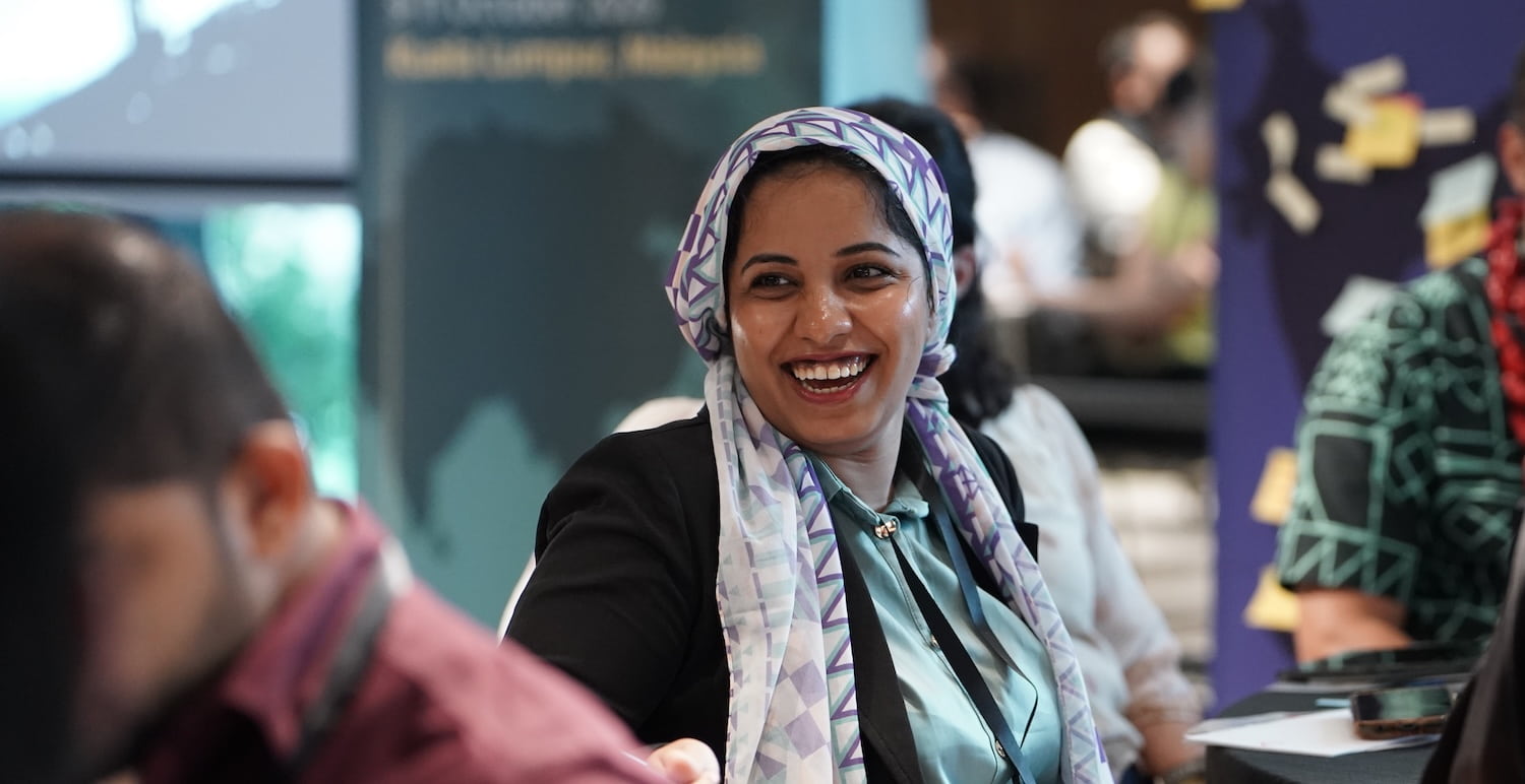 A woman in a headscarf smiles warmly while seated at a table