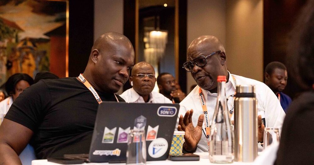 Two men wearing orange lanyards sit and talk