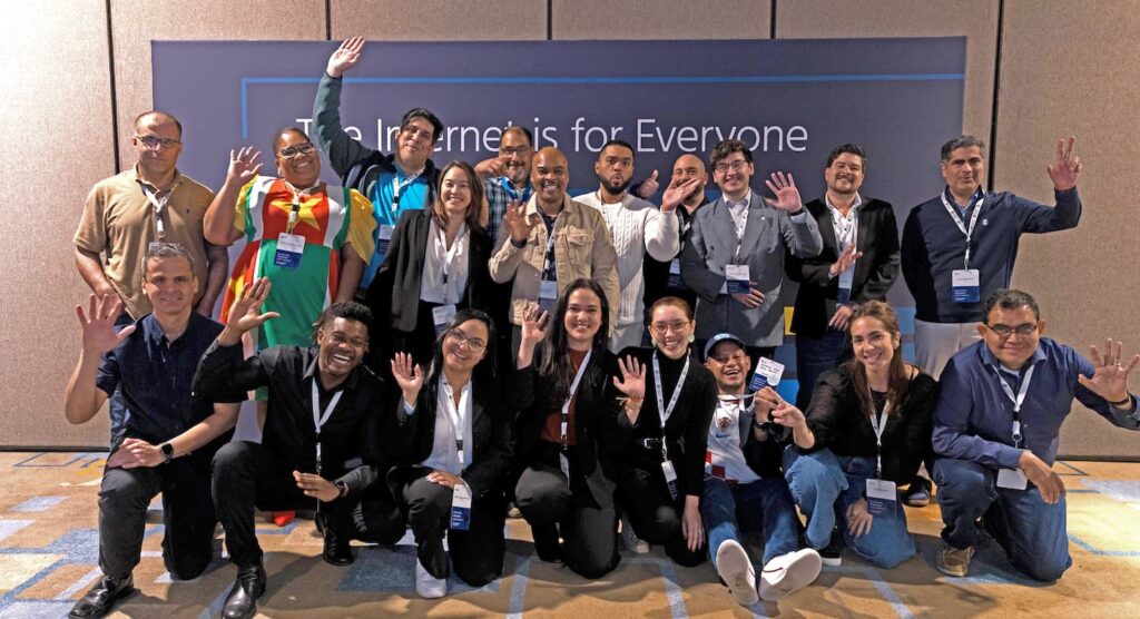 A group of people smile and throw up peace signs and thumbs up.