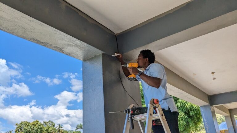 A man stands on a ladder and holds a drill, installing infrastructure