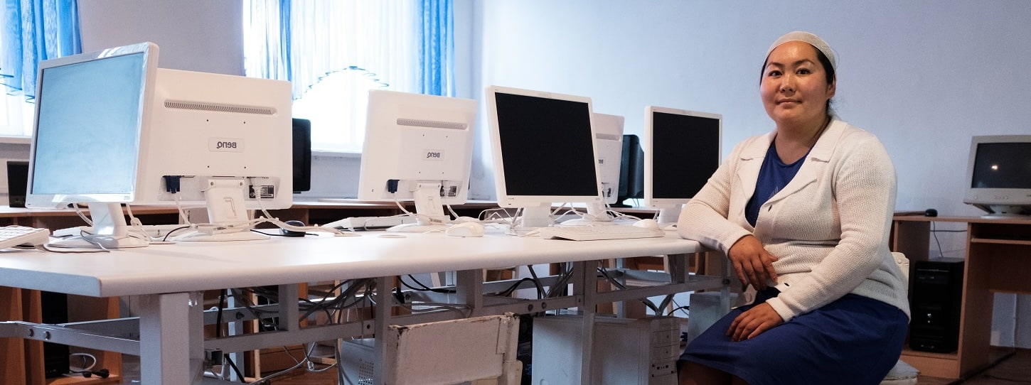 A woman seated at a desk with many computer screens in the background